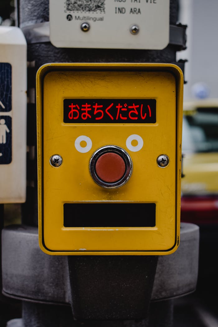 Yellow pedestrian signal button with Japanese text on a city street corner.