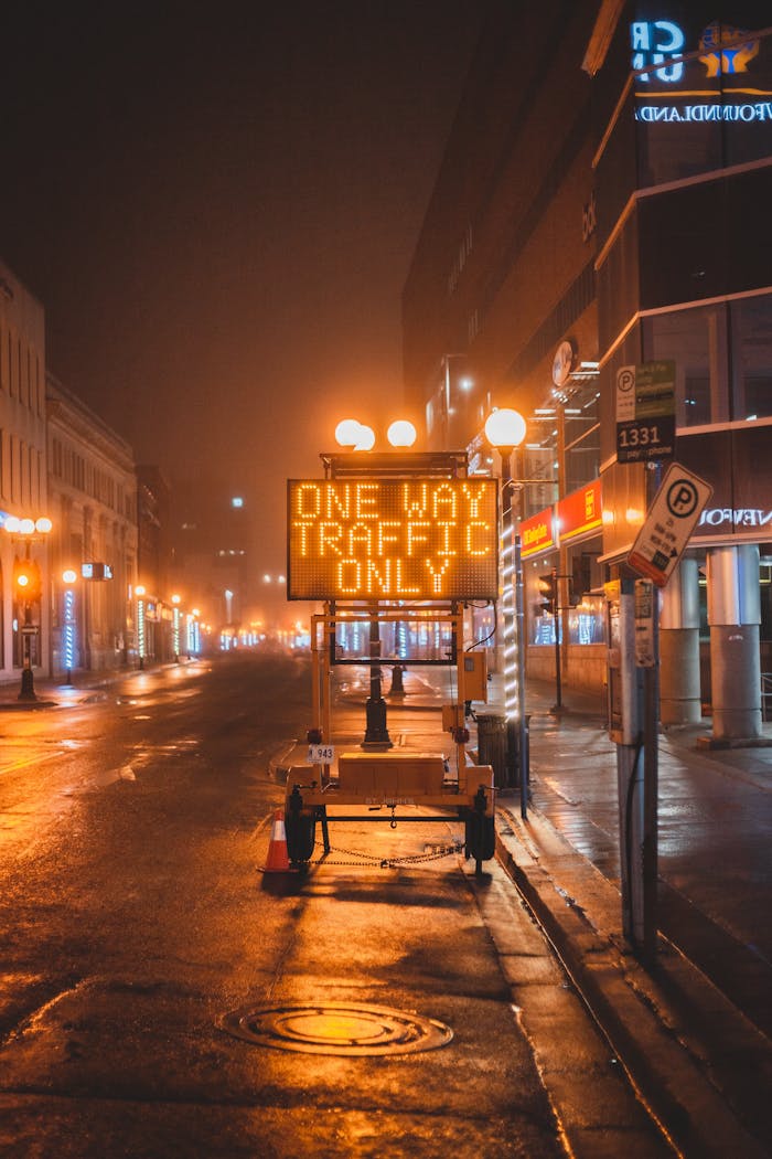 Mobile electronic sign with inscription One way traffic only placed on wet asphalt road on street in city in night time